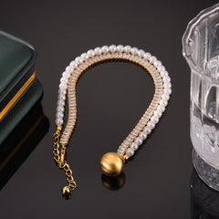 Necklace featuring pearl-spliced chain and gold sphere pendant on neutral background