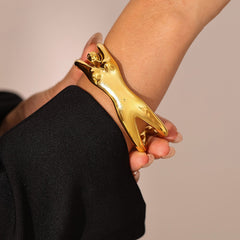 Side view of exaggerated gold cuff bracelet reflecting soft light
