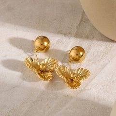 Flat lay of gold floral dome earrings beside perfume and pearl necklace