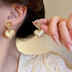 Close-up of floral heart-shaped gold earrings with pearl center