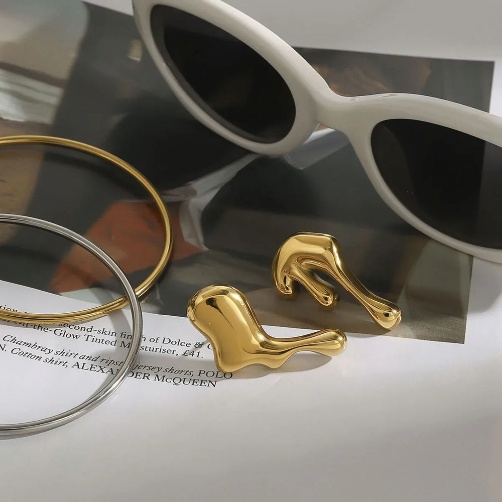 Gold sculptural earrings styled on neutral stone background