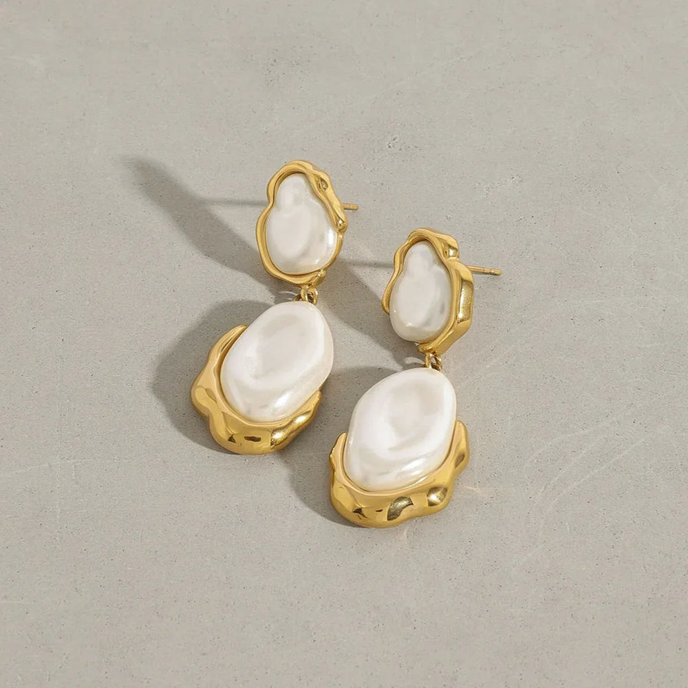 Pair of irregular pearl earrings laid next to seashells and gold jewelry box