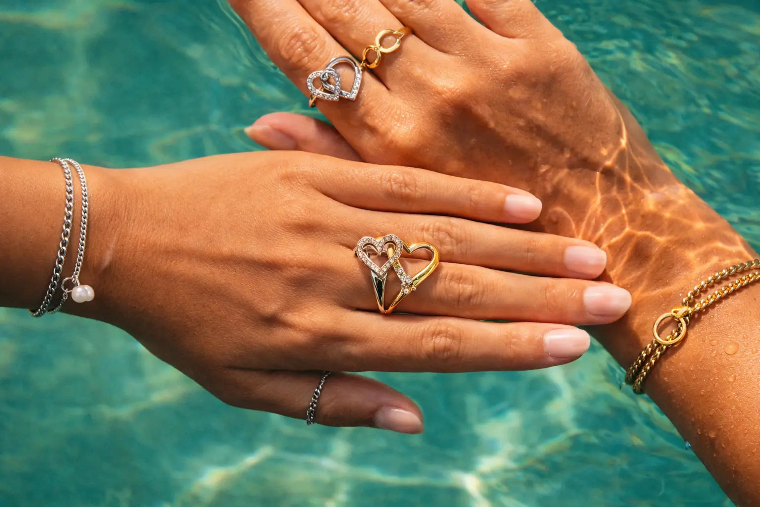 Two hands with heart-shaped rings on a blurred water background