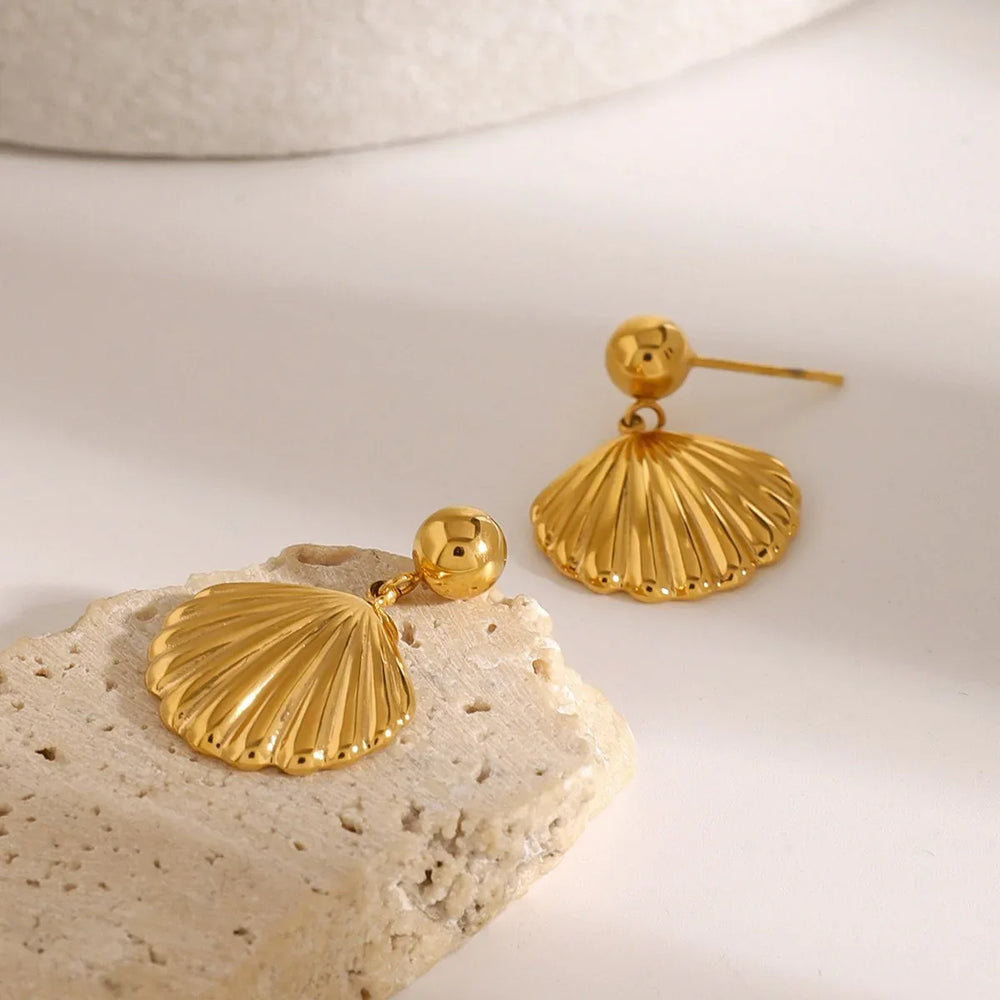 Flat lay of Solenne gold earrings with shell accents beside other gold jewelry